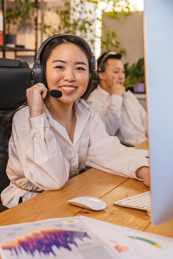 Smiling employees at call center desk using headsets and computers.